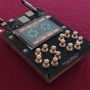 Puede incluir: Dispositivo electrónico negro con una pantalla que muestra un gráfico colorido. Tiene perillas doradas y una base de madera. El texto "Wildwood Lightning v2.2" es visible en el dispositivo.