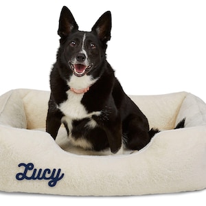 Black and white dog on cream faux fur personalized dog bed cover embroidered with the name Lucy; removable, washable, and soft, this custom dog bed accessory makes a cozy calming dog bed and doubles as stylish pet furniture for homes.