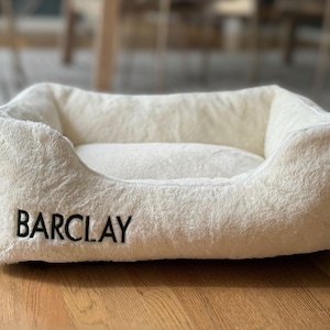 Soft white faux fur personalized dog bed cover embroidered with the name Barclay; removable and washable, this cozy cover transforms a standard dog bed into a custom dog bed or calming dog bed, making it both stylish pet furniture and a thoughtful pet owner gift or dog birthday gift.
