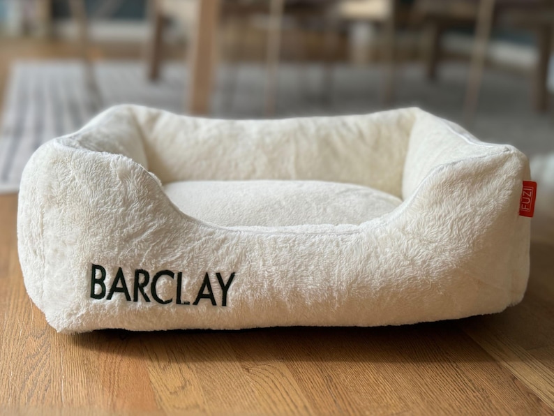 Soft white faux fur personalized dog bed cover embroidered with the name Barclay; removable and washable, this cozy cover transforms a standard dog bed into a custom dog bed or calming dog bed, making it both stylish pet furniture and a thoughtful pet owner gift or dog birthday gift.