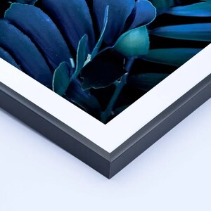 May include: A framed print featuring a close-up of dark blue and teal leaves. The artwork is set within a black frame with a white mat, creating a modern and elegant aesthetic. The leaves have a glossy appearance.