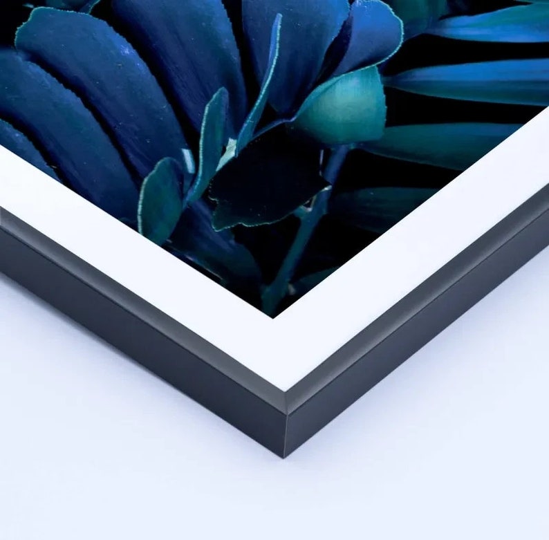 May include: A framed print featuring a close-up of dark blue and teal leaves. The artwork is set within a black frame with a white mat, creating a modern and elegant aesthetic. The leaves have a glossy appearance.