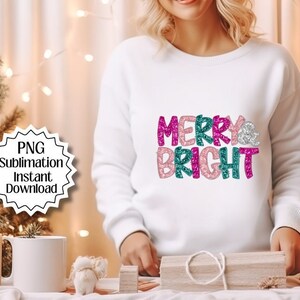 May include: White sweatshirt with the text "Merry & Bright" in pink, teal, and silver glitter lettering.