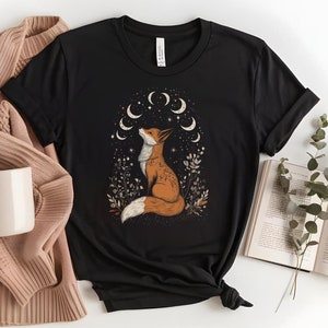 Op de afbeelding: Zwart T-shirt met een afbeelding van een vos die onder een halve maan met sterren zit. De vos is oranje en wit met een borstelige staart.