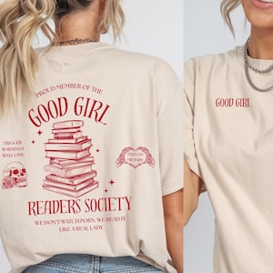 Peut inclure: T-shirt beige avec l'inscription rouge "GOOD GIRL" à l'avant et à l'arrière. Le dos présente une pile de livres, une tête de mort et le texte "READERS SOCIETY".