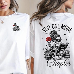 Op de afbeelding: Wit T-shirt met een zwart-witte illustratie van een skelet dat een boek leest met een rode roos. De tekst "Just One More Chapter" is op het T-shirt gedrukt.