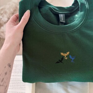 Embroidered dragon book sweatshirt for fantasy book lovers, cozy bookish dragon crewneck with detailed dragon embroidery. Perfect gift for readers, BookTok fans, librarians and fantasy readers. Aesthetic book lover sweatshirt inspired by dragons and magical stories, ideal bookish merch for reading lovers, dragon readers and fantasy literature fans.