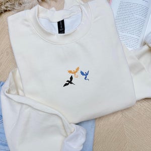 Embroidered dragon book sweatshirt for fantasy book lovers, cozy bookish dragon crewneck with detailed dragon embroidery. Perfect gift for readers, BookTok fans, librarians and fantasy readers. Aesthetic book lover sweatshirt inspired by dragons and magical stories, ideal bookish merch for reading lovers, dragon readers and fantasy literature fans.