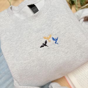 Embroidered dragon book sweatshirt for fantasy book lovers, cozy bookish dragon crewneck with detailed dragon embroidery. Perfect gift for readers, BookTok fans, librarians and fantasy readers. Aesthetic book lover sweatshirt inspired by dragons and magical stories, ideal bookish merch for reading lovers, dragon readers and fantasy literature fans.