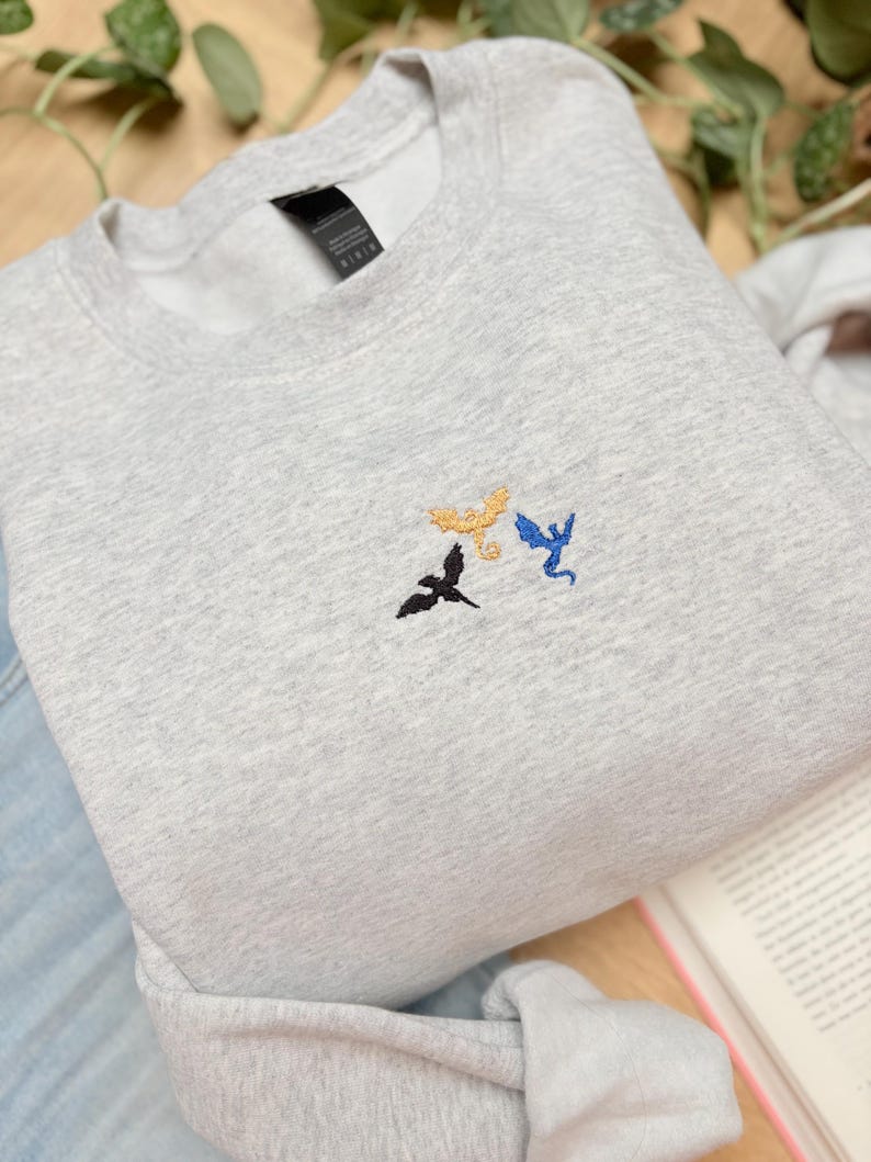Embroidered dragon book sweatshirt for fantasy book lovers, cozy bookish dragon crewneck with detailed dragon embroidery. Perfect gift for readers, BookTok fans, librarians and fantasy readers. Aesthetic book lover sweatshirt inspired by dragons and magical stories, ideal bookish merch for reading lovers, dragon readers and fantasy literature fans.