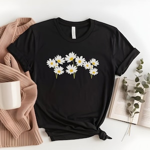 Op de afbeelding: Een zwart T-shirt met een witte madeliefjesprint. De madeliefjes zijn in een cluster gerangschikt en hebben gele centra.