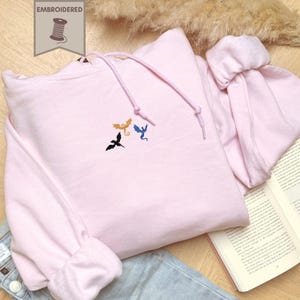 Embroidered dragon book sweatshirt for fantasy book lovers, cozy bookish dragon crewneck with detailed dragon embroidery. Perfect gift for readers, BookTok fans, librarians and fantasy readers. Aesthetic book lover sweatshirt inspired by dragons and magical stories, ideal bookish merch for reading lovers, dragon readers and fantasy literature fans.