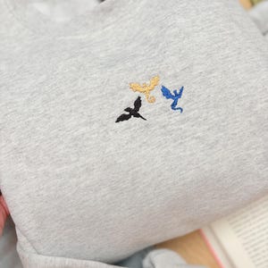 Embroidered dragon book sweatshirt for fantasy book lovers, cozy bookish dragon crewneck with detailed dragon embroidery. Perfect gift for readers, BookTok fans, librarians and fantasy readers. Aesthetic book lover sweatshirt inspired by dragons and magical stories, ideal bookish merch for reading lovers, dragon readers and fantasy literature fans.