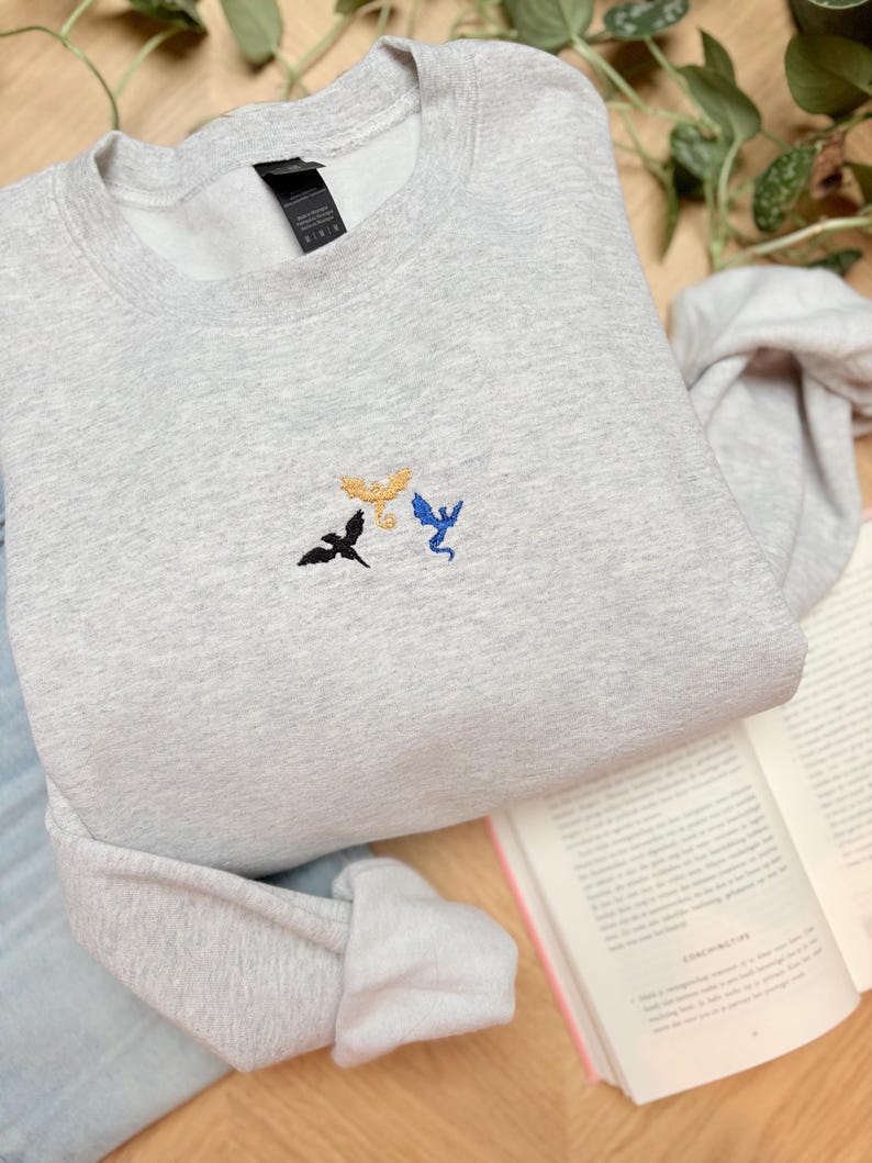 Embroidered dragon book sweatshirt for fantasy book lovers, cozy bookish dragon crewneck with detailed dragon embroidery. Perfect gift for readers, BookTok fans, librarians and fantasy readers. Aesthetic book lover sweatshirt inspired by dragons and magical stories, ideal bookish merch for reading lovers, dragon readers and fantasy literature fans.