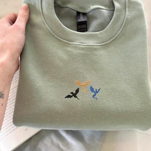 Embroidered dragon book sweatshirt for fantasy book lovers, cozy bookish dragon crewneck with detailed dragon embroidery. Perfect gift for readers, BookTok fans, librarians and fantasy readers. Aesthetic book lover sweatshirt inspired by dragons and magical stories, ideal bookish merch for reading lovers, dragon readers and fantasy literature fans.