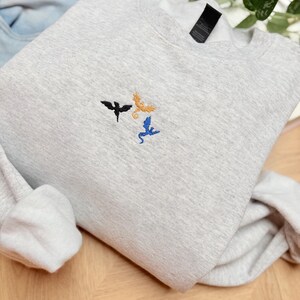 Embroidered dragon book sweatshirt for fantasy book lovers, cozy bookish dragon crewneck with detailed dragon embroidery. Perfect gift for readers, BookTok fans, librarians and fantasy readers. Aesthetic book lover sweatshirt inspired by dragons and magical stories, ideal bookish merch for reading lovers, dragon readers and fantasy literature fans.