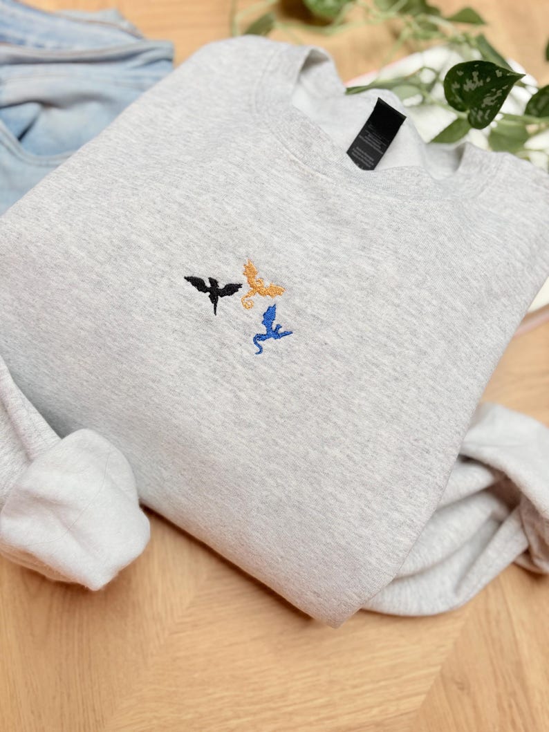 Embroidered dragon book sweatshirt for fantasy book lovers, cozy bookish dragon crewneck with detailed dragon embroidery. Perfect gift for readers, BookTok fans, librarians and fantasy readers. Aesthetic book lover sweatshirt inspired by dragons and magical stories, ideal bookish merch for reading lovers, dragon readers and fantasy literature fans.