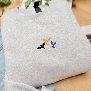 Embroidered dragon book sweatshirt for fantasy book lovers, cozy bookish dragon crewneck with detailed dragon embroidery. Perfect gift for readers, BookTok fans, librarians and fantasy readers. Aesthetic book lover sweatshirt inspired by dragons and magical stories, ideal bookish merch for reading lovers, dragon readers and fantasy literature fans.