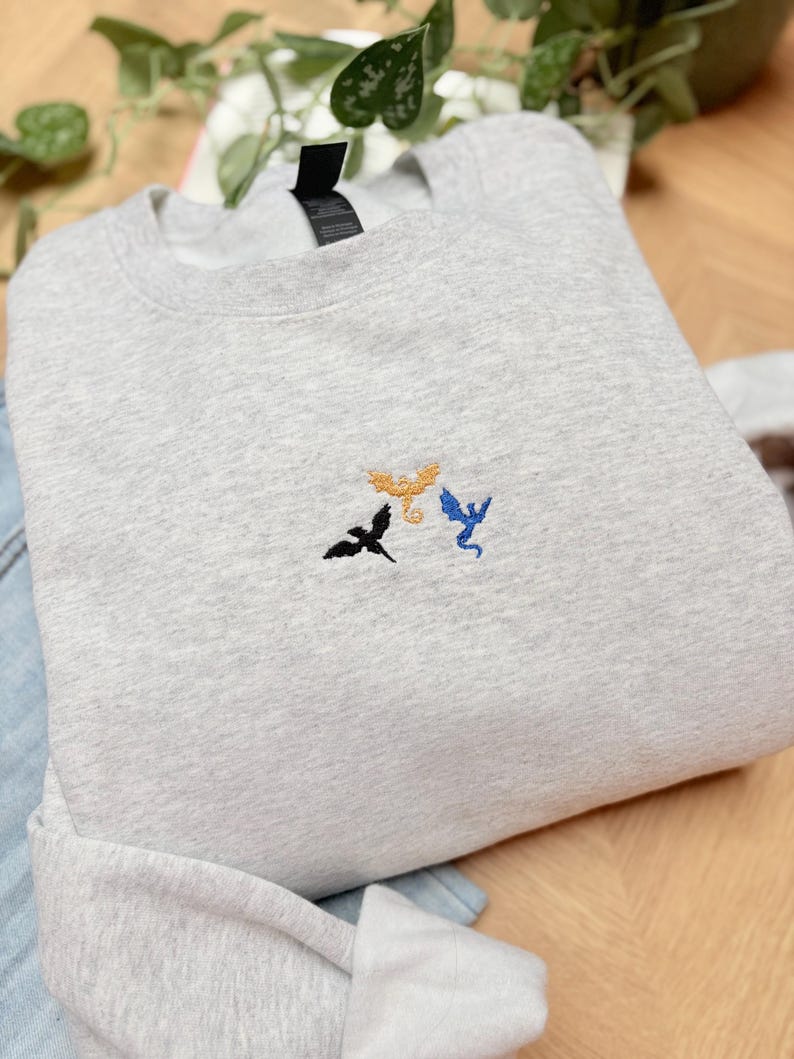 Embroidered dragon book sweatshirt for fantasy book lovers, cozy bookish dragon crewneck with detailed dragon embroidery. Perfect gift for readers, BookTok fans, librarians and fantasy readers. Aesthetic book lover sweatshirt inspired by dragons and magical stories, ideal bookish merch for reading lovers, dragon readers and fantasy literature fans.