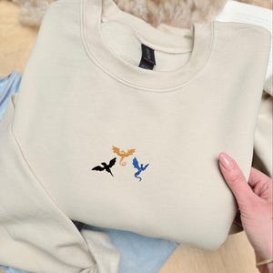 Embroidered dragon book sweatshirt for fantasy book lovers, cozy bookish dragon crewneck with detailed dragon embroidery. Perfect gift for readers, BookTok fans, librarians and fantasy readers. Aesthetic book lover sweatshirt inspired by dragons and magical stories, ideal bookish merch for reading lovers, dragon readers and fantasy literature fans.