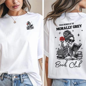 Pode incluir: Camiseta branca com um esqueleto lendo um livro e segurando uma rosa vermelha nas costas. A frente da camiseta tem um pequeno gráfico de um esqueleto lendo um livro. O texto nas costas diz "Proud Member of the Morally Grey Book Club".