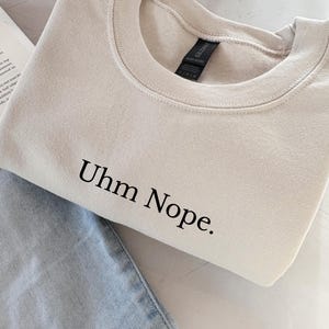 Geborduurd sweatshirt met de tekst “Uhm Nope.” in een minimalistisch lettertype. De trui heeft een comfortabele pasvorm en een rustige, stijlvolle uitstraling. Het ontwerp straalt humor, zelfbeschikking en duidelijke grenzen uit. Geschikt voor casual outfits, relaxmomenten of als origineel cadeau voor iemand die vandaag gewoon even nee zegt.