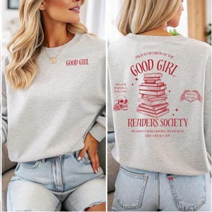 Peut inclure: Un sweat-shirt gris clair avec le texte "GOOD GIRL" en rouge sur le devant. Le dos du sweat-shirt pr&eacute;sente une pile de livres, un cr&acirc;ne et les mots "PROUD MEMBER OF THE GOOD GIRL READERS SOCIETY".