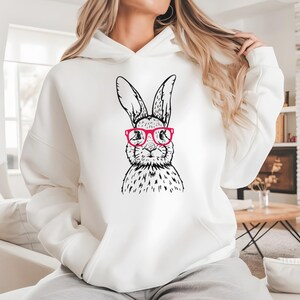 Può includere: Felpa bianca con un'illustrazione in bianco e nero di un coniglio con occhiali rosa.