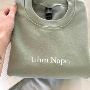 Geborduurd sweatshirt met de tekst “Uhm Nope.” in een minimalistisch lettertype. De trui heeft een comfortabele pasvorm en een rustige, stijlvolle uitstraling. Het ontwerp straalt humor, zelfbeschikking en duidelijke grenzen uit. Geschikt voor casual outfits, relaxmomenten of als origineel cadeau voor iemand die vandaag gewoon even nee zegt.