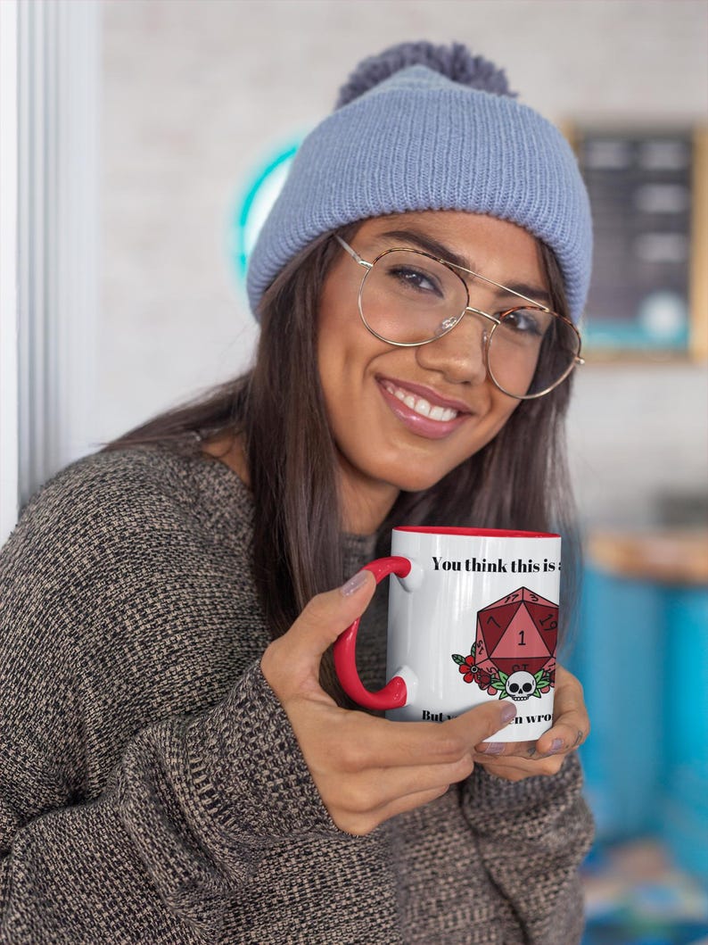 May include: White ceramic mug with a red interior and handle. The mug features the text "You think this is" and a graphic of a red D20 die, flowers, and a skull. The mug is a novelty item.