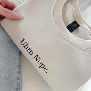 Geborduurd sweatshirt met de tekst “Uhm Nope.” in een minimalistisch lettertype. De trui heeft een comfortabele pasvorm en een rustige, stijlvolle uitstraling. Het ontwerp straalt humor, zelfbeschikking en duidelijke grenzen uit. Geschikt voor casual outfits, relaxmomenten of als origineel cadeau voor iemand die vandaag gewoon even nee zegt.