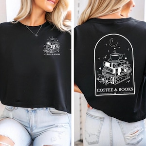 Op de afbeelding: Zwart gecropped T-shirt met een witte afbeelding van een stapel boeken, een kopje koffie en een halve maan met sterren. De tekst "COFFEE & BOOKS" is op het shirt gedrukt.