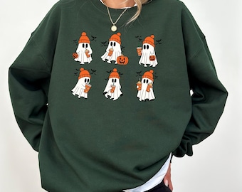 May include: Dark green sweatshirt featuring a Halloween-themed design. The graphic includes six cartoon ghosts wearing orange beanies and holding coffee cups. A pumpkin and bats are also part of the design. The sweatshirt has a crew neck and long sleeves.