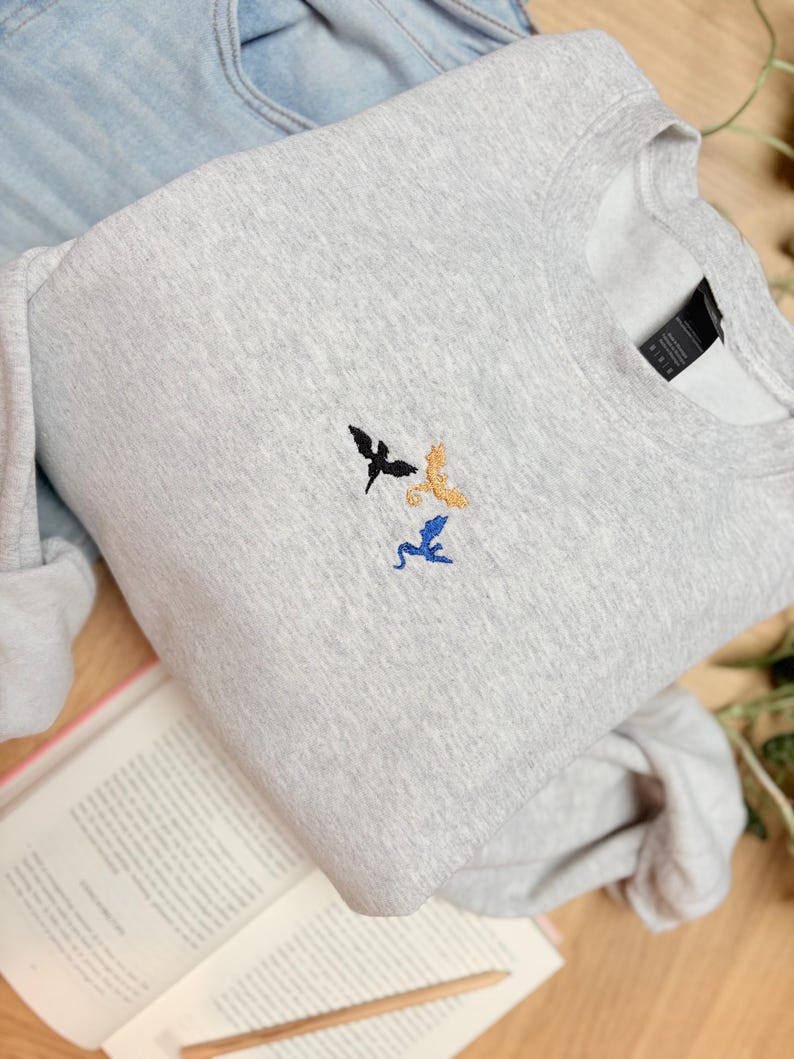 Embroidered dragon book sweatshirt for fantasy book lovers, cozy bookish dragon crewneck with detailed dragon embroidery. Perfect gift for readers, BookTok fans, librarians and fantasy readers. Aesthetic book lover sweatshirt inspired by dragons and magical stories, ideal bookish merch for reading lovers, dragon readers and fantasy literature fans.
