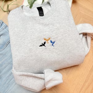 Embroidered dragon book sweatshirt for fantasy book lovers, cozy bookish dragon crewneck with detailed dragon embroidery. Perfect gift for readers, BookTok fans, librarians and fantasy readers. Aesthetic book lover sweatshirt inspired by dragons and magical stories, ideal bookish merch for reading lovers, dragon readers and fantasy literature fans.