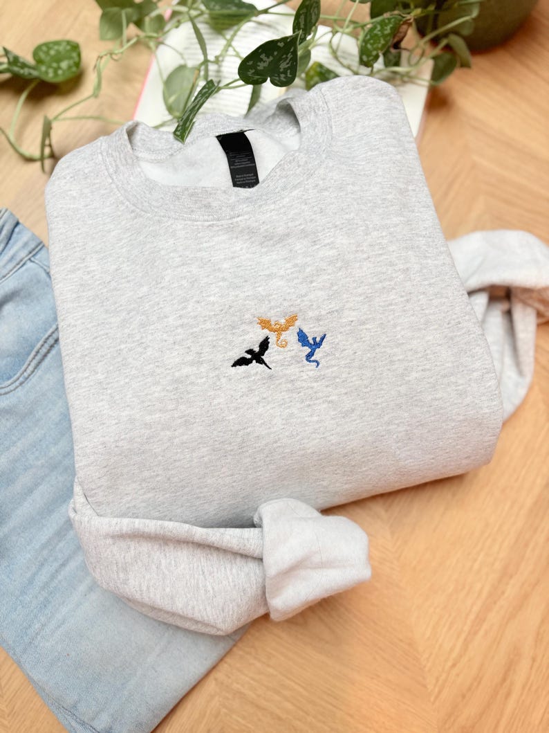 Embroidered dragon book sweatshirt for fantasy book lovers, cozy bookish dragon crewneck with detailed dragon embroidery. Perfect gift for readers, BookTok fans, librarians and fantasy readers. Aesthetic book lover sweatshirt inspired by dragons and magical stories, ideal bookish merch for reading lovers, dragon readers and fantasy literature fans.