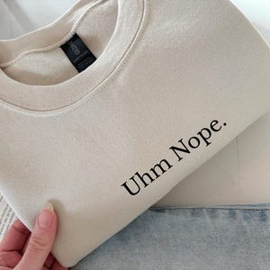 Geborduurd sweatshirt met de tekst “Uhm Nope.” in een minimalistisch lettertype. De trui heeft een comfortabele pasvorm en een rustige, stijlvolle uitstraling. Het ontwerp straalt humor, zelfbeschikking en duidelijke grenzen uit. Geschikt voor casual outfits, relaxmomenten of als origineel cadeau voor iemand die vandaag gewoon even nee zegt.