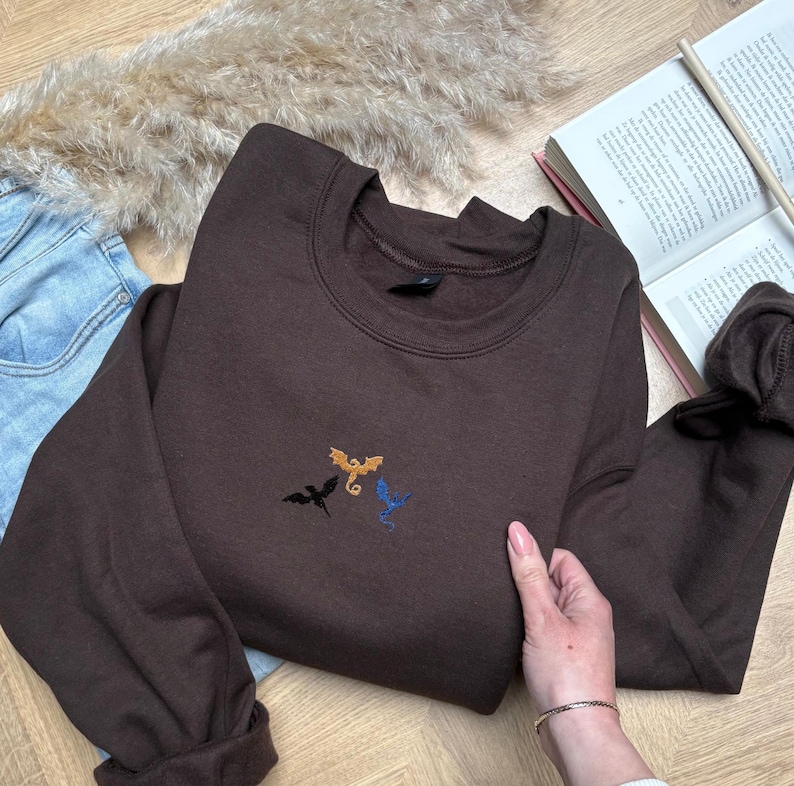 Embroidered dragon book sweatshirt for fantasy book lovers, cozy bookish dragon crewneck with detailed dragon embroidery. Perfect gift for readers, BookTok fans, librarians and fantasy readers. Aesthetic book lover sweatshirt inspired by dragons and magical stories, ideal bookish merch for reading lovers, dragon readers and fantasy literature fans.