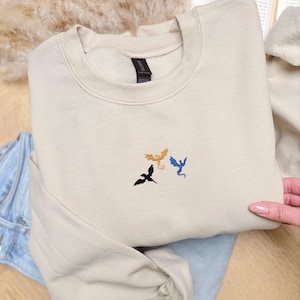 Embroidered dragon book sweatshirt for fantasy book lovers, cozy bookish dragon crewneck with detailed dragon embroidery. Perfect gift for readers, BookTok fans, librarians and fantasy readers. Aesthetic book lover sweatshirt inspired by dragons and magical stories, ideal bookish merch for reading lovers, dragon readers and fantasy literature fans.