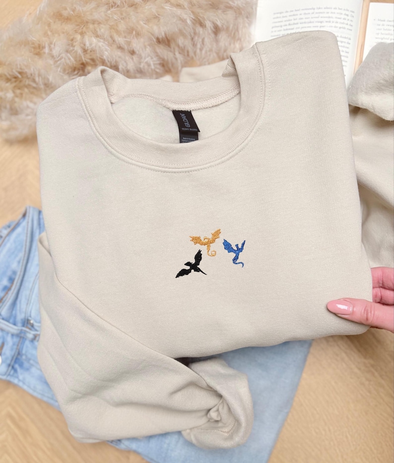 Embroidered dragon book sweatshirt for fantasy book lovers, cozy bookish dragon crewneck with detailed dragon embroidery. Perfect gift for readers, BookTok fans, librarians and fantasy readers. Aesthetic book lover sweatshirt inspired by dragons and magical stories, ideal bookish merch for reading lovers, dragon readers and fantasy literature fans.