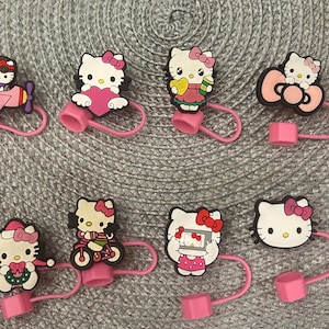 May include: A selection of Hello Kitty bottle stoppers. Each stopper has a pink base and a Hello Kitty figure in different poses and outfits. One stopper has the text "HELLO COFFEE". The stoppers are designed to fit bottles.