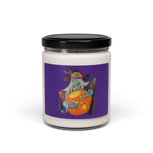 Puede incluir: Un tarro de vela blanco con tapa negra. La etiqueta presenta una ilustración vintage de una bruja de piel verde con un sombrero negro sosteniendo una linterna de calabaza naranja sobre un fondo púrpura. Un artículo decorativo con temática de Halloween.