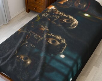 May include: A dark-colored blanket featuring a repeating pattern of ornate, golden masks. The masks have intricate details and are set against a dark background. The blanket is draped over a bed, with a wooden nightstand visible in the background.