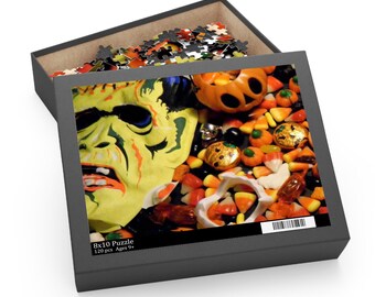 May include: A Halloween-themed puzzle in a black box. The puzzle image features a Frankenstein monster, candy corn, and jack-o'-lanterns. The box reads "8x10 Puzzle 120 pcs Ages 9+".