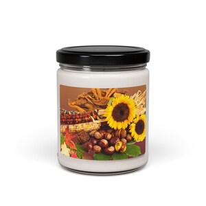 May include: A glass jar candle with a brown, white, and yellow label featuring a still life of sunflowers, corn, and chestnuts.