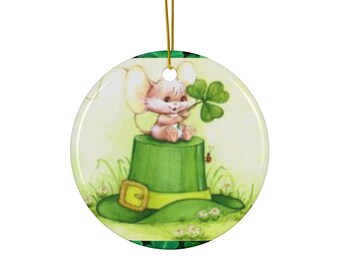 Peut inclure: Une décoration en céramique représentant une souris de dessin animé portant un chapeau de lutin vert et tenant un trèfle à quatre feuilles. La décoration est ornée de trèfles verts et d'un fond blanc.