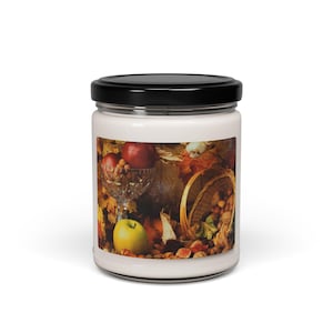 Puede incluir: Una vela en un tarro de vidrio con una tapa negra y una etiqueta que presenta una naturaleza muerta de frutas, nueces y hojas en colores otoñales.