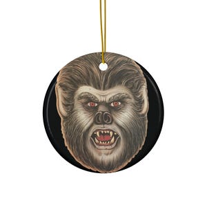 May include: A round ceramic ornament featuring a close-up of a werewolf's face with sharp teeth and red eyes. The werewolf is depicted with a snarling expression against a black background.