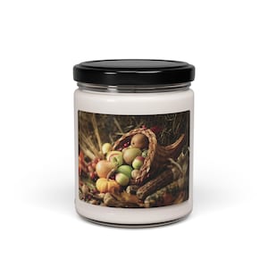 Puede incluir: Un tarro de vela blanco con tapa negra. La etiqueta presenta una cornucopia rebosante de frutas y verduras de otoño, incluyendo manzanas, peras y calabazas.
