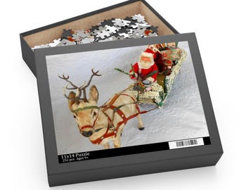 May include: A Christmas-themed puzzle in a black box, featuring Santa Claus in a sleigh pulled by a reindeer. The puzzle image shows a detailed scene with a white background. The box is labeled "11x14 Puzzle" with "252 pcs Ages 9+".